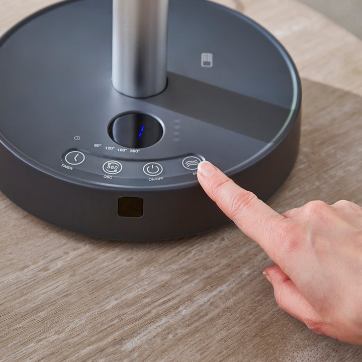 Person pressing a button on a black fan on a wooden surface