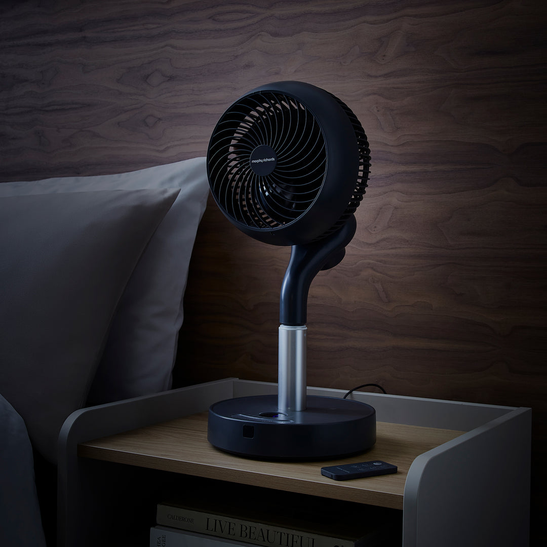 Black oscillating table fan on a nightstand with a wooden wall background