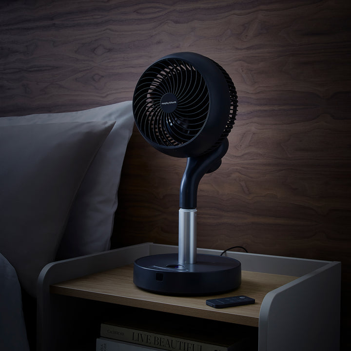 Black oscillating table fan on a nightstand with a wooden wall background