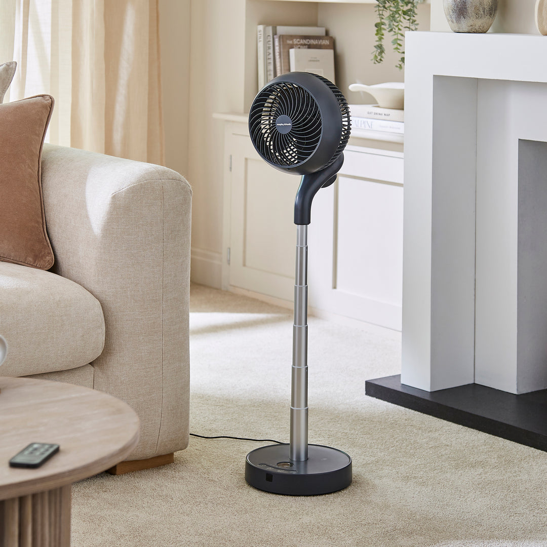 Black standing fan in a living room setting with a couch and coffee table.