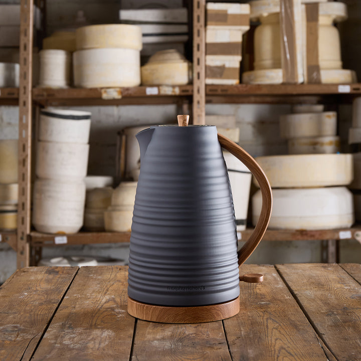 Dark gray electric kettle with wooden handle on a wooden table in a warehouse setting