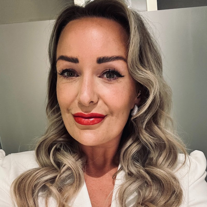 Woman with wavy blonde hair and red lipstick wearing a white top.