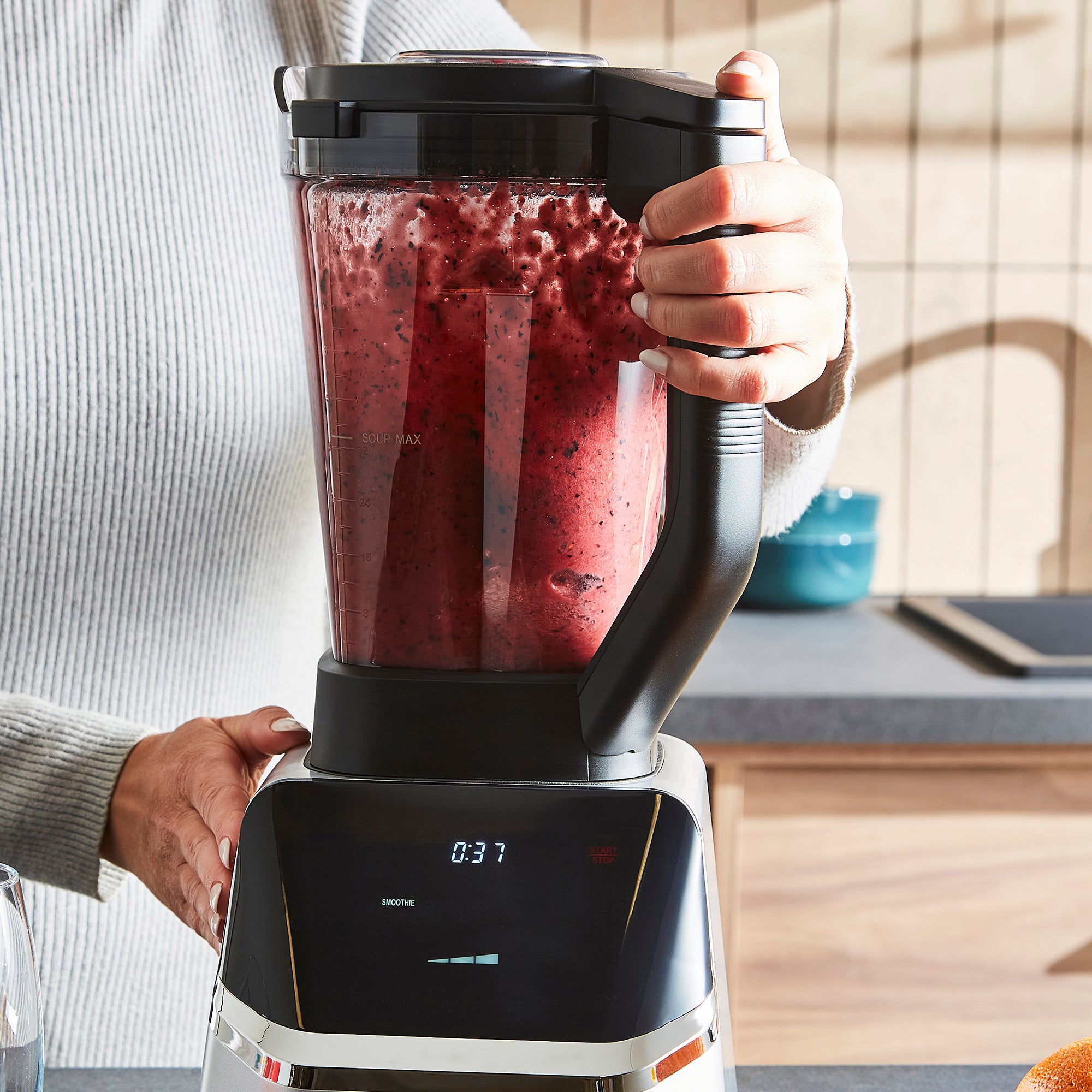 Person holding a blender with a red smoothie inside, kitchen setting