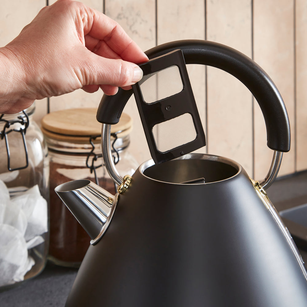 Person adjusting a filter in a black kettle with a wooden background