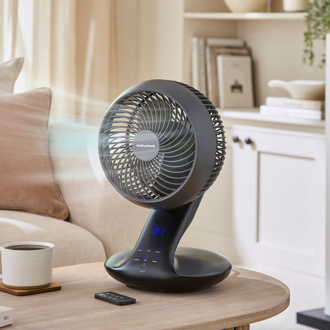 Tabletop fan on a wooden table with a remote control in a living room setting.