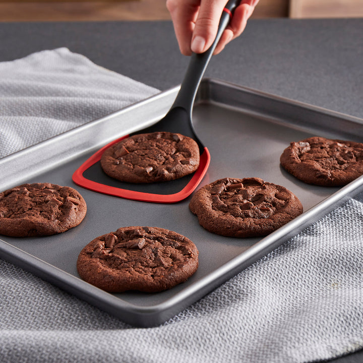 Chocolate cookies on a baking tray with a spatula lifting one cookie.