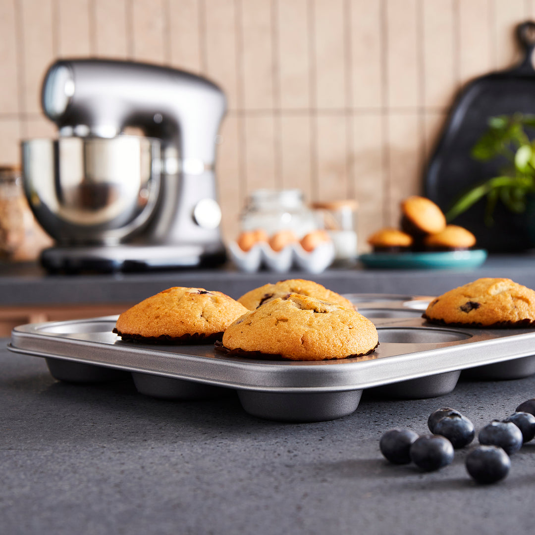 Muffin tray with baked muffins on a kitchen counter, mixer in the background