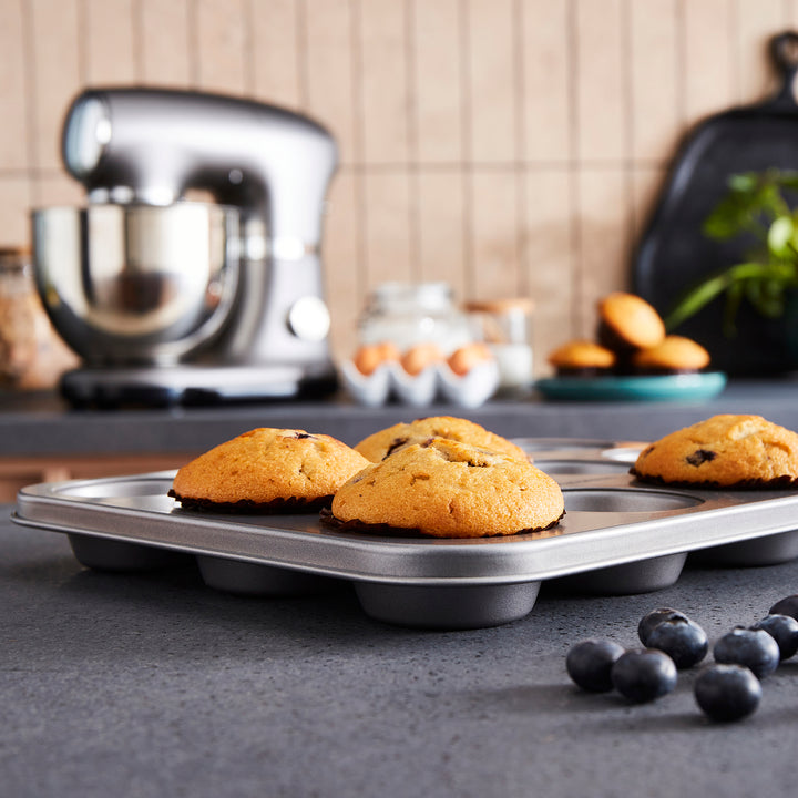 Muffin tray with baked muffins on a kitchen counter, mixer in the background