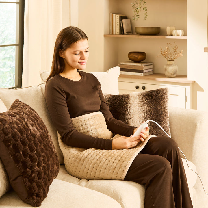 Woman sitting on sofa with large heat pad over stomach.