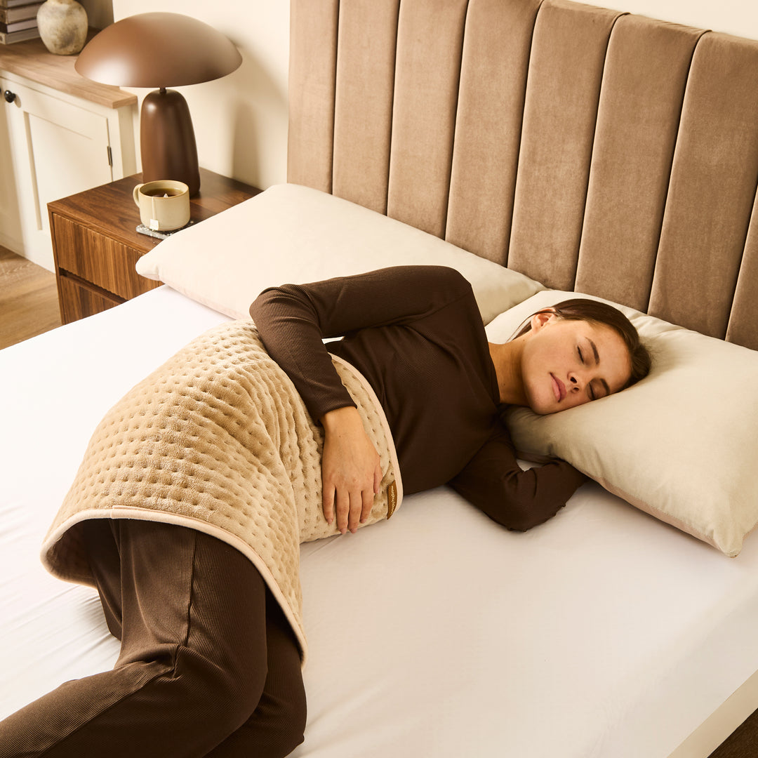 Woman sleeping on a bed with a beige large heat pad.