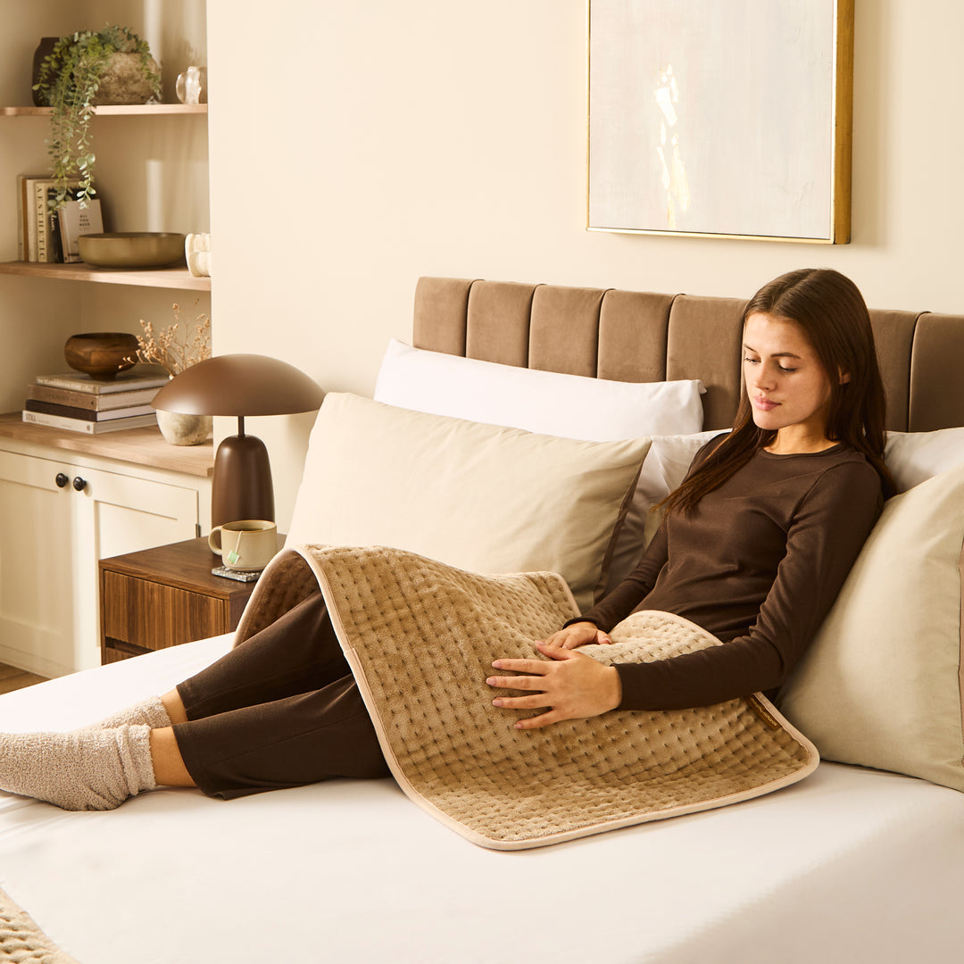 Woman sitting on a bed with a heat pad over legs