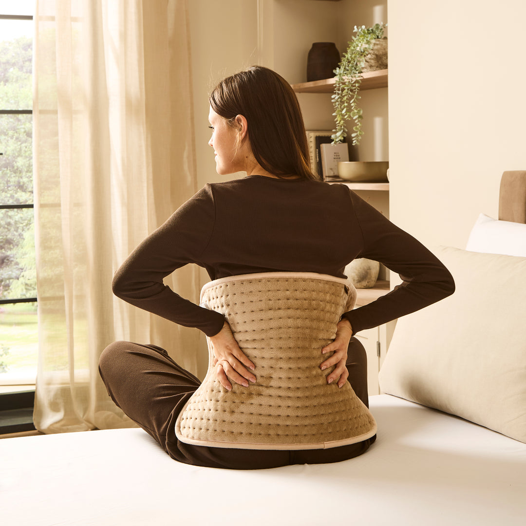 Woman in bedroom using heat pad to sooth back pain