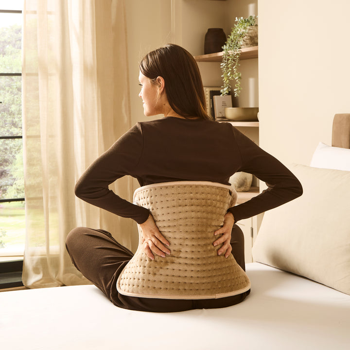 Woman in bedroom using heat pad to sooth back pain