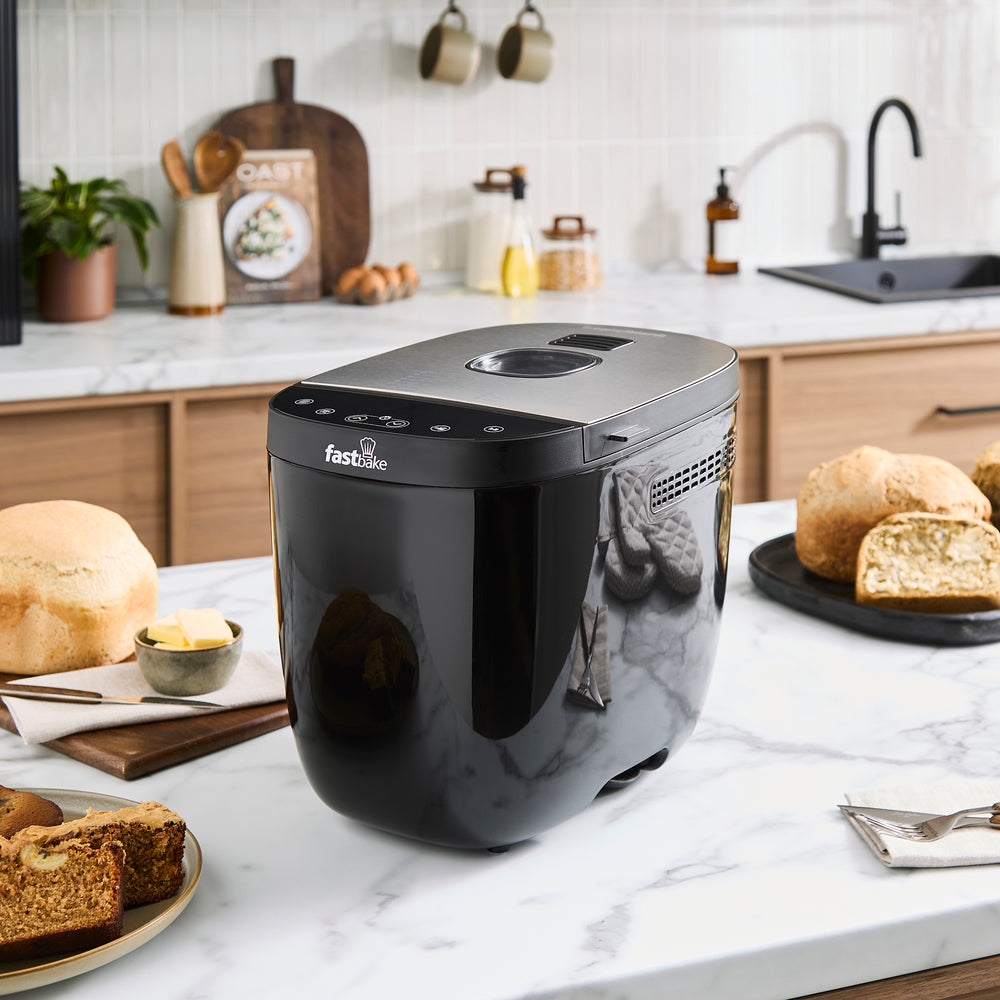 Black bread maker on a kitchen counter with bread and butter