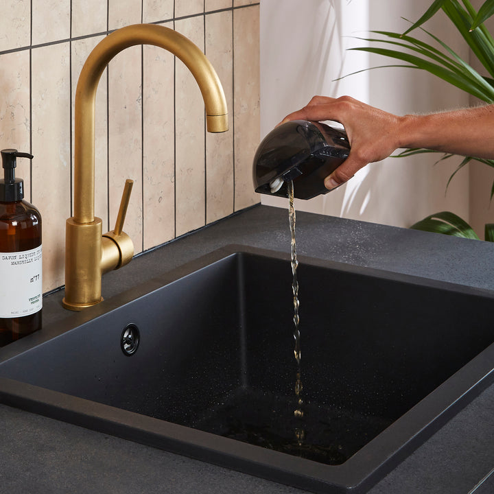 Person pouring water from a black container into a black sink with a gold faucet.