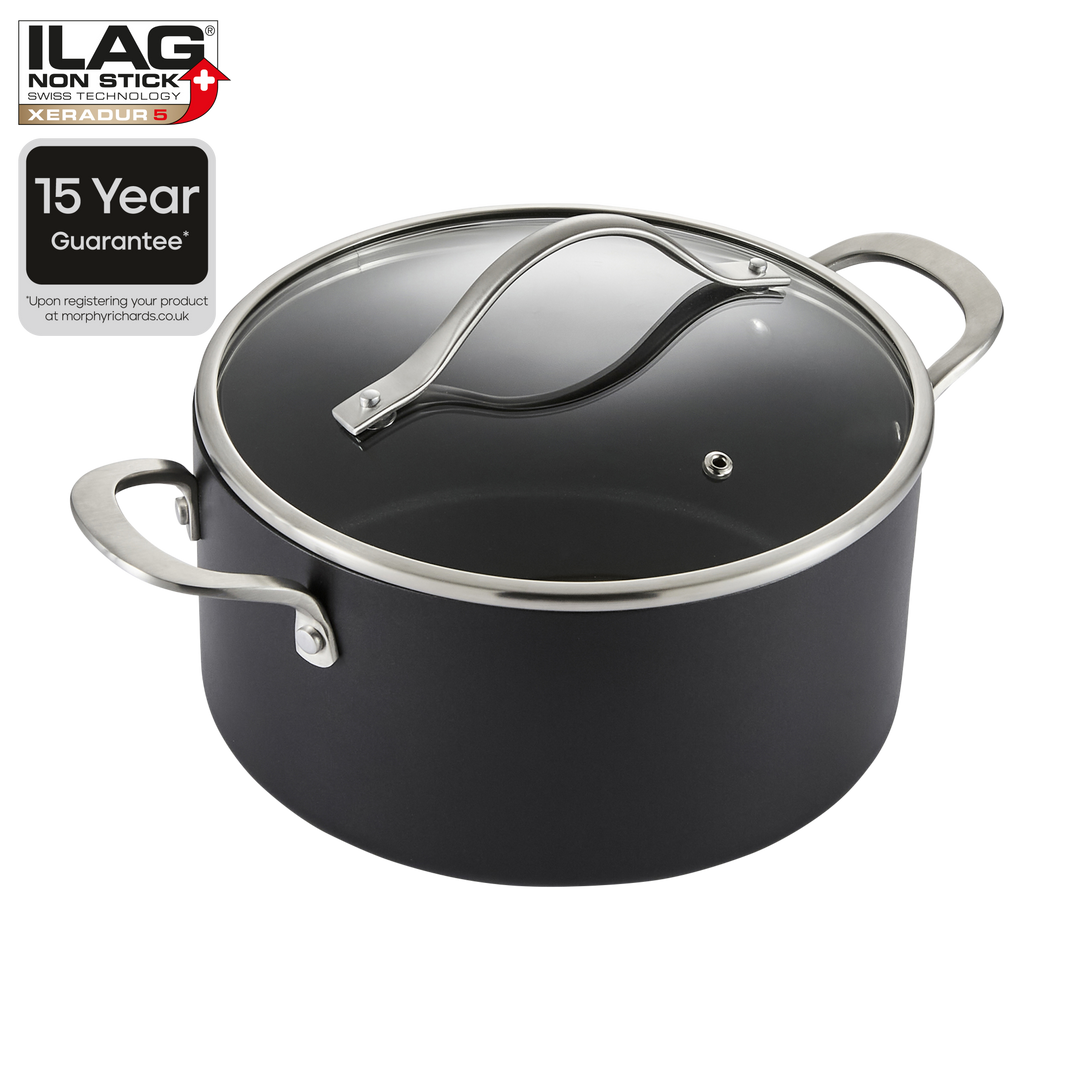 A black non-stick saucepan with a clear glass lid and silver metal handles, shown on a white background with an ILAG Non-Stick 15 Year Guarantee badge in the top-left corner.