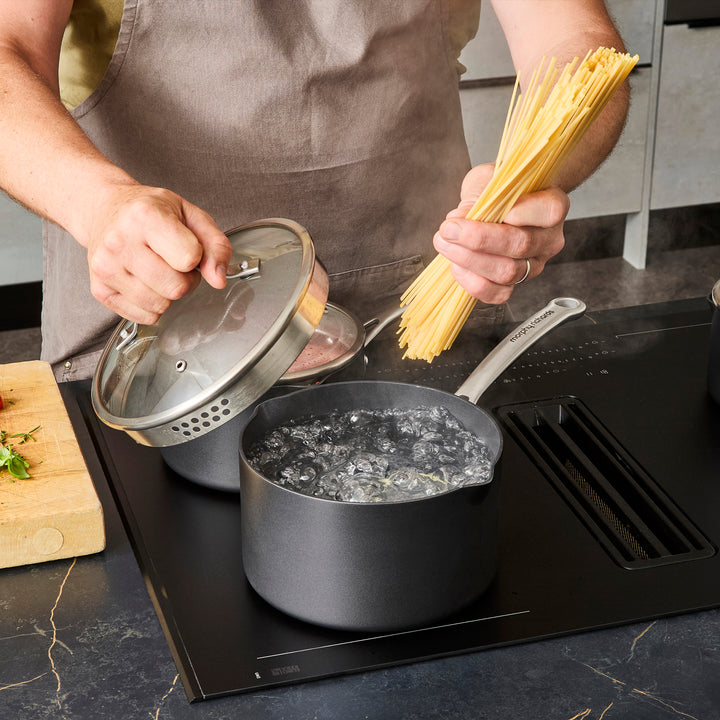 Saucepan full of boiling water on induction hob, adding pasta to the water