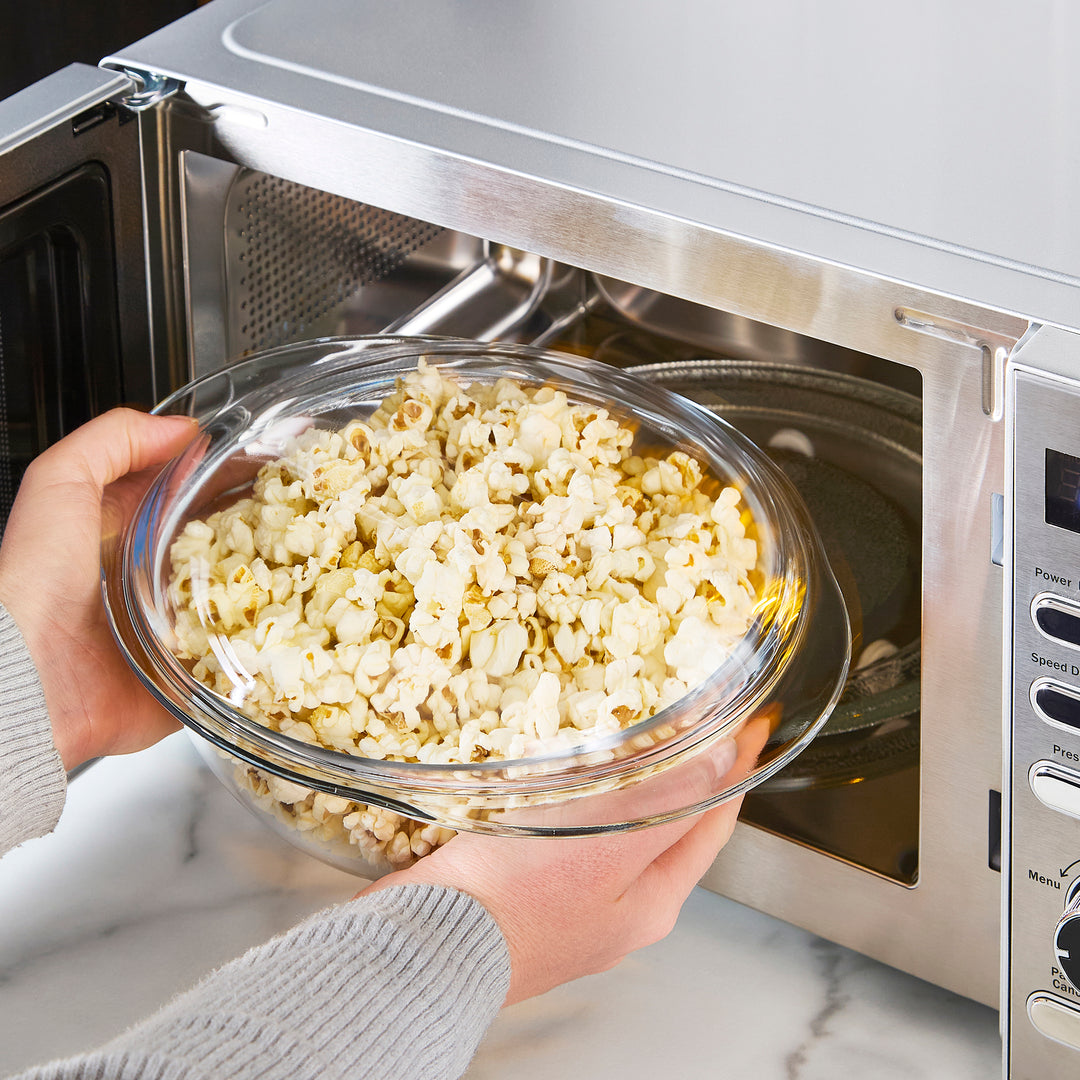 A stainless steel microwave oven sitting on a white marble kitchen countertop against a white tiled backsplash.