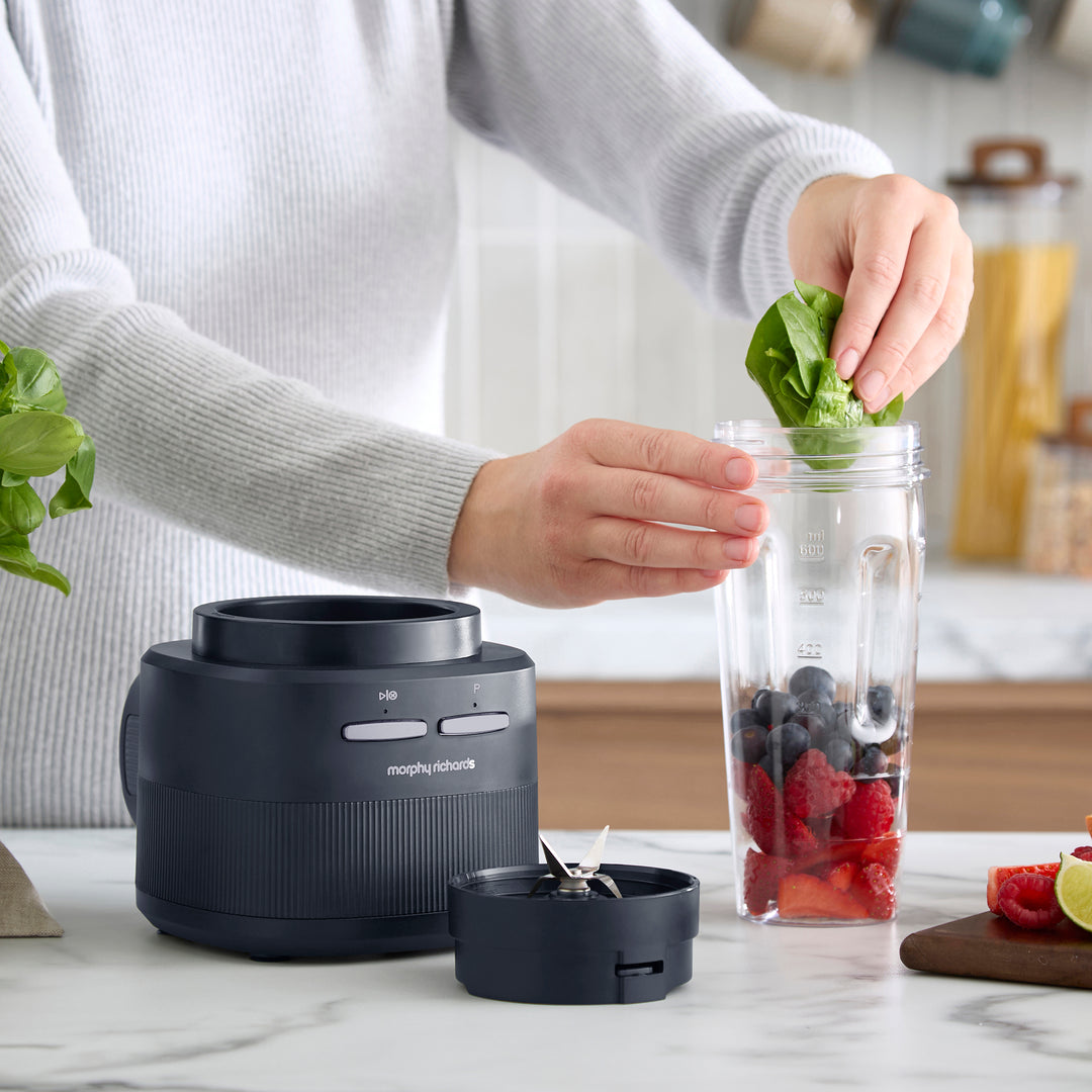 A person adding spinach leaves into a cordless blender
