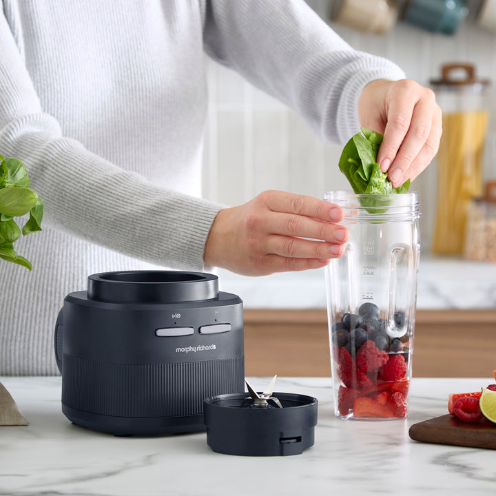A person adding spinach leaves into a cordless blender
