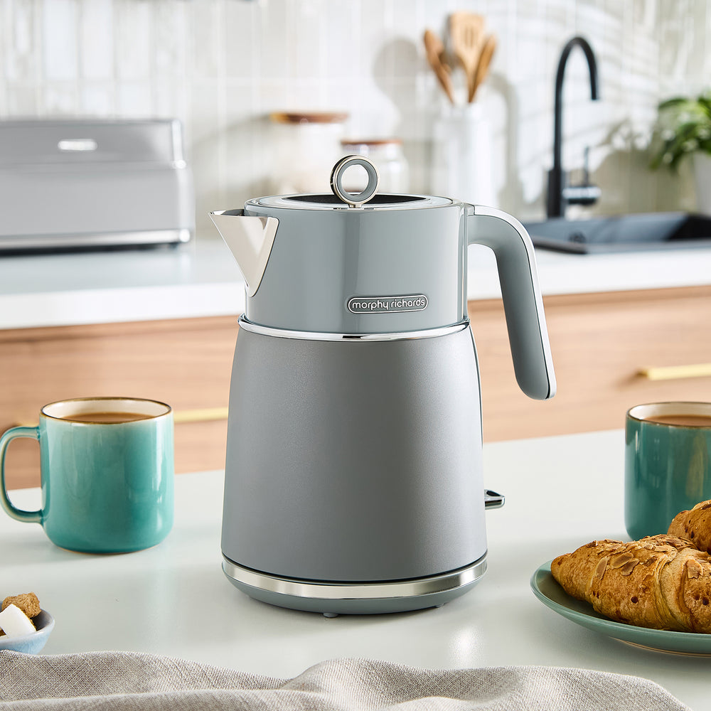 Grey kettle on a kitchen counter with two teal mugs and pastries.