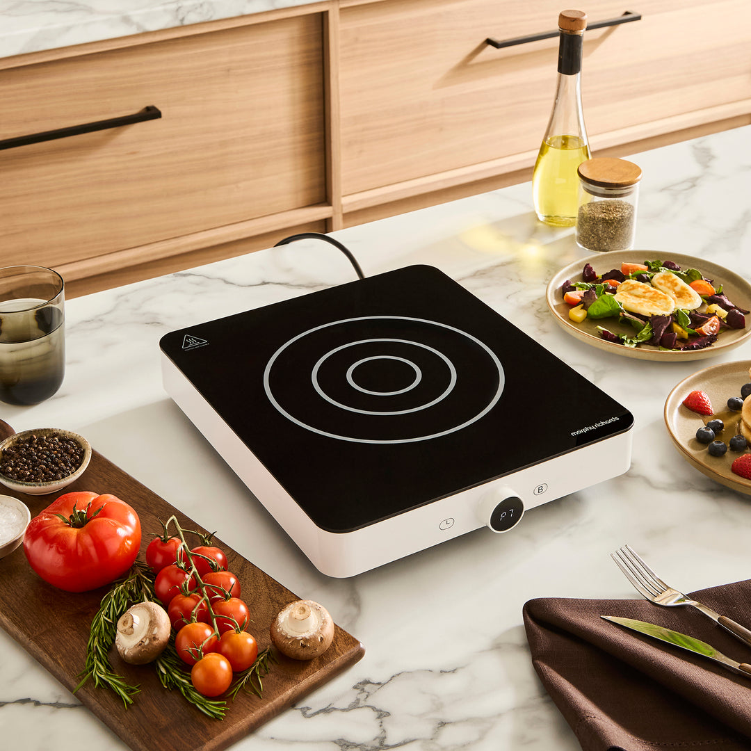Portable induction cooktop on a kitchen counter with food and utensils around