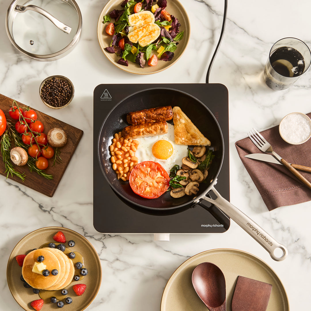 single induction hob with frying pan on top filled with full english breakfast ingredients