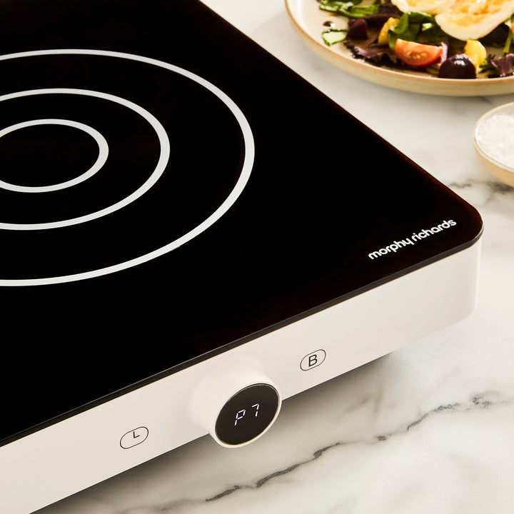 Black induction cooker with white spiral heating element on a marble countertop.