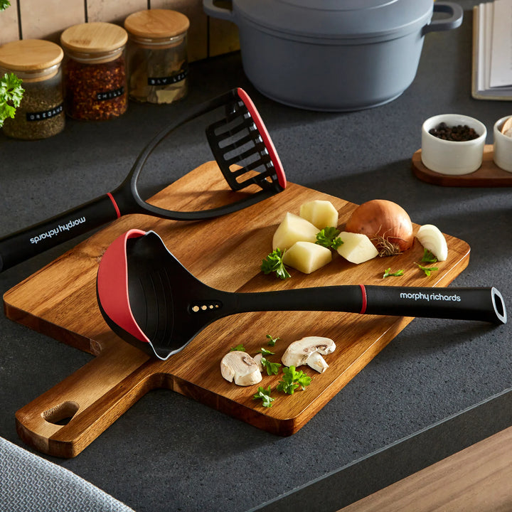Morphy Richards kitchen utensils on a wooden cutting board with vegetables on a kitchen counter.