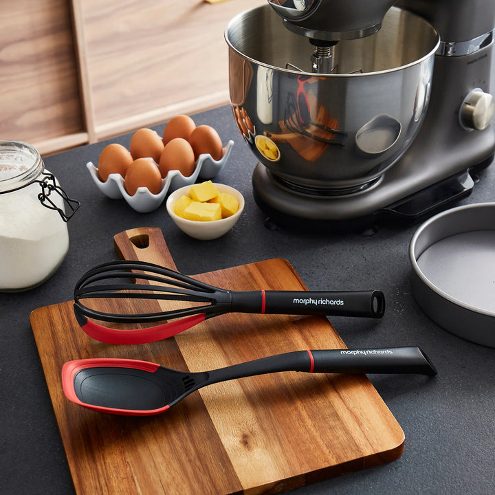 Morphy Richards kitchen utensils on a wooden cutting board with vegetables on a kitchen counter.