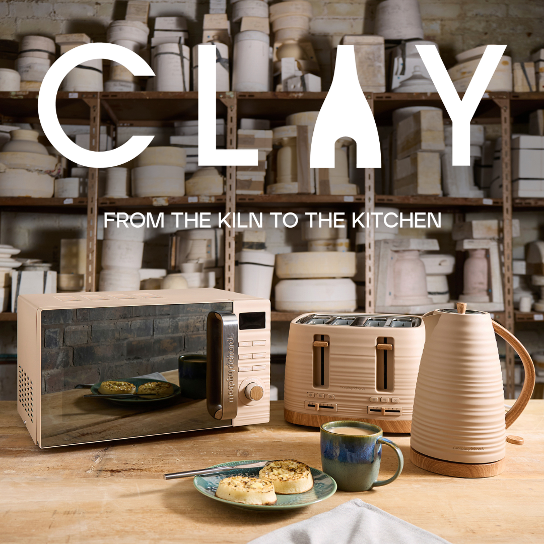Ceramic kitchen appliances and items on a table with shelves of pottery in the background, featuring the brand 'CLAY'.