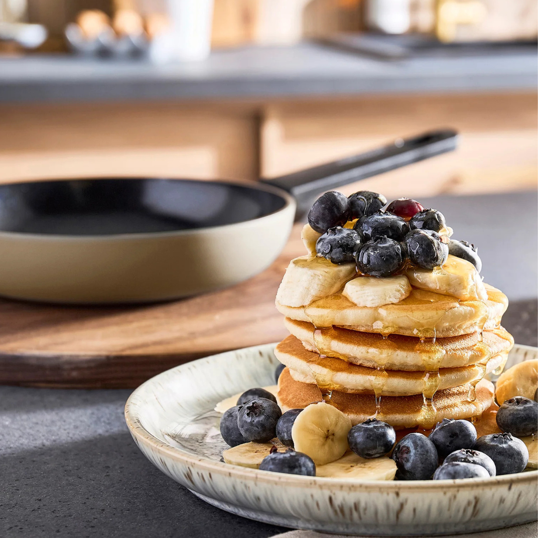 Stack of pancakes with blueberries and bananas on a plate in a kitchen setting.